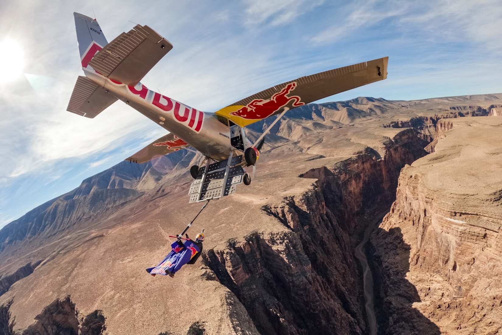 A man attached to a plane flying over a canyon.