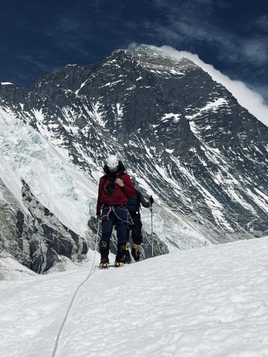 Climbers clipped to a rope on a snow slope, with the summit of Everest behind them.