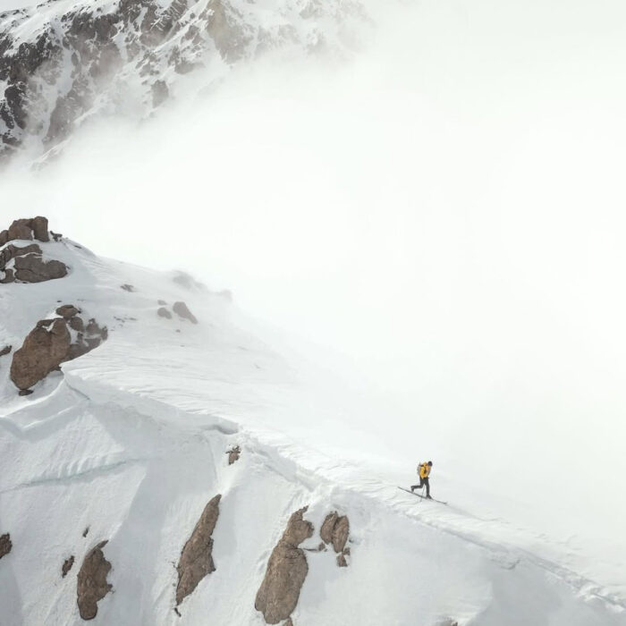 Herve Barmasse on skis along a snowy ridge in a foggy day.