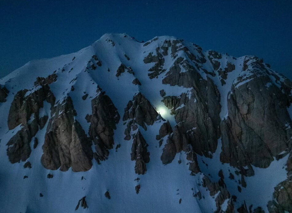 The light of a climber's headlamp illuminates the snowy face of Italy's Grand Sasso in the night.