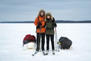 two skiers standing beside sleds on the snow