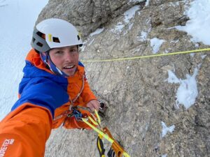 The climber takes a selfie while auto-belaying with a jumar on a mixed wall.