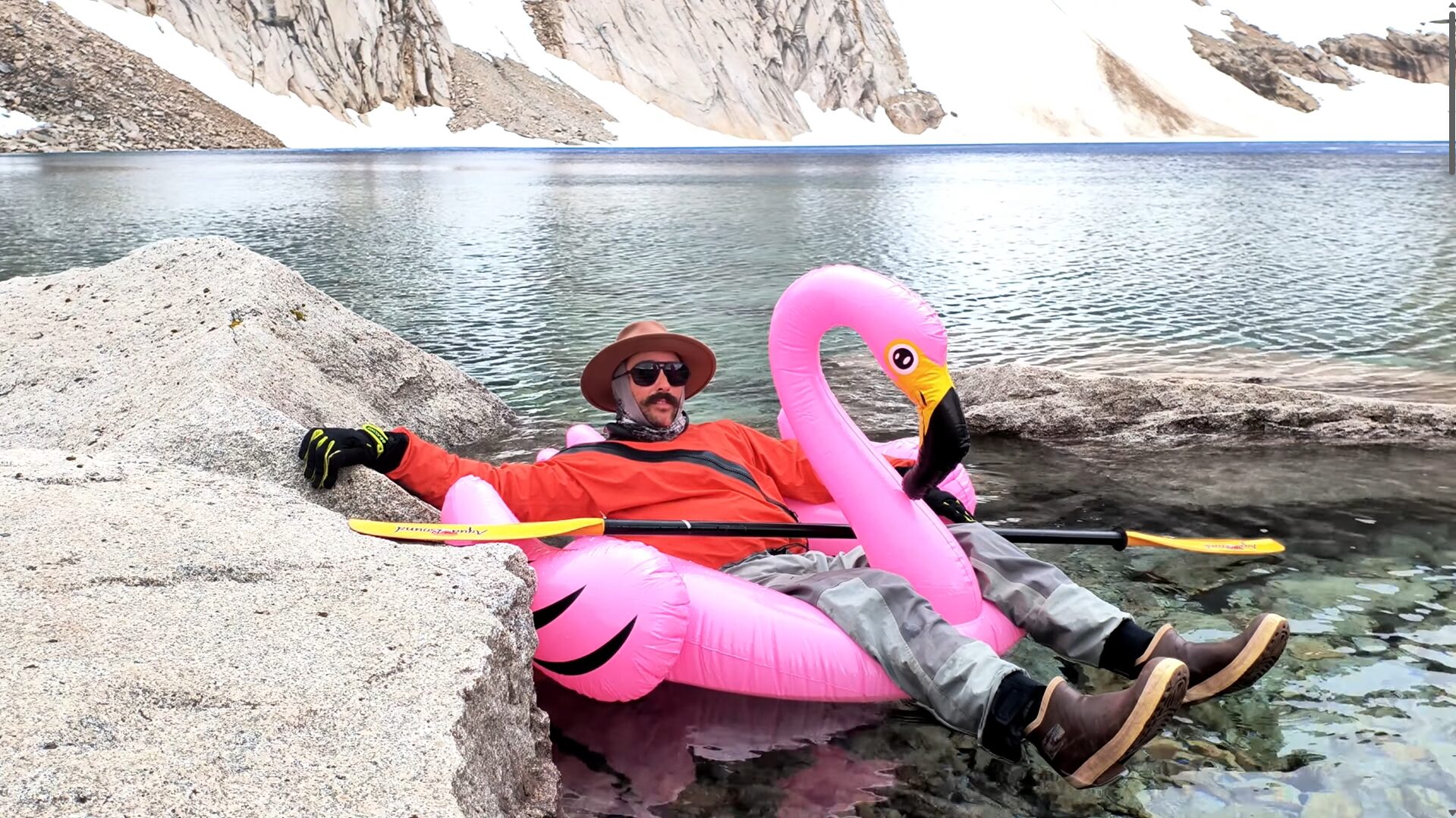 A man sitting in a lake on an inflatable pink flamingo.