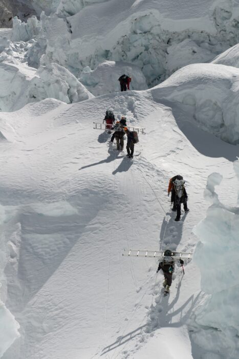 Sherps walking in line on the snow among seracs and crevases. 