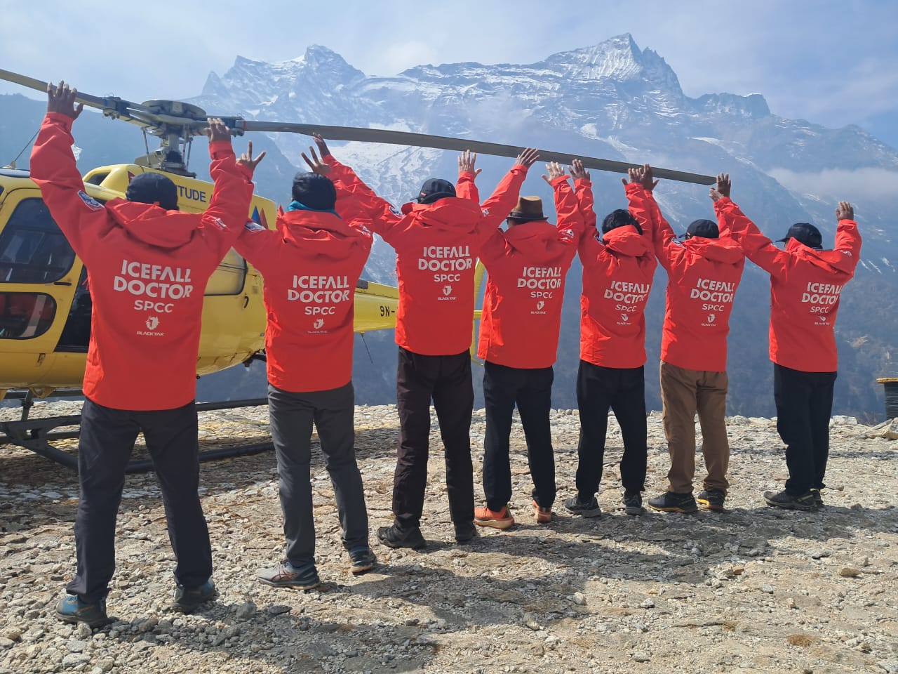 The ICefall Doctors pose with their uniform jackets in front of a helicopter