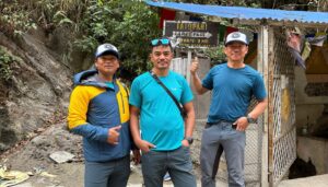 Prakash Guring and mebers in his team pose by the dirt road with a sign directing to Tatopani