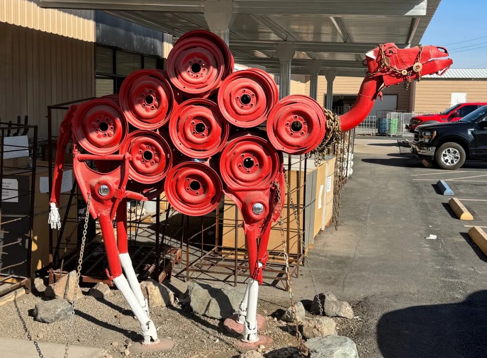 A sculpture made of discarded car parts, shaped like a camel and painted bright red.