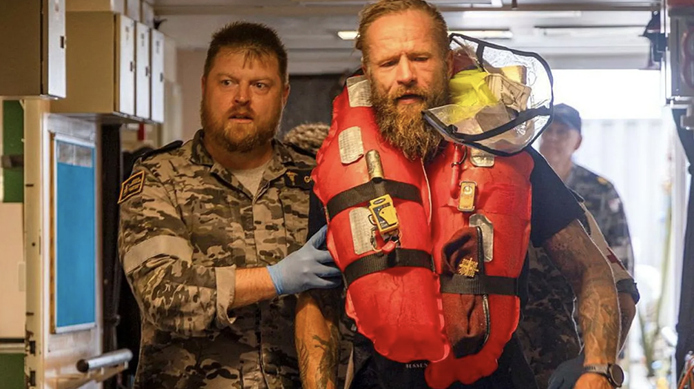 bearded man in life jacket helped by ailor