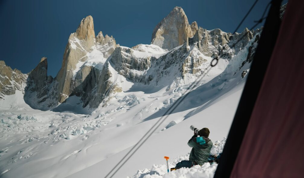 A man pointing a camera at a snowy mountaintop