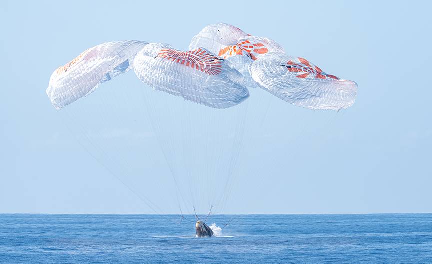 space capsule under parachute splashes down