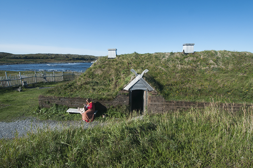 woman in Viking dress outside replica Viking longhouse, L'Anse aux Meadows, Newfoundland.