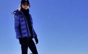 Anja Blacha poses on a snow slope on a mountain with the sky as background.