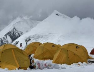 Yellow tents on the snow at Dhaulagiri, with snowy peaks and cloudy sky in foreground.