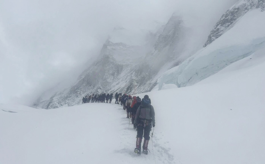 Climbers in line on a snow plateau at Everest, in a foggy day.