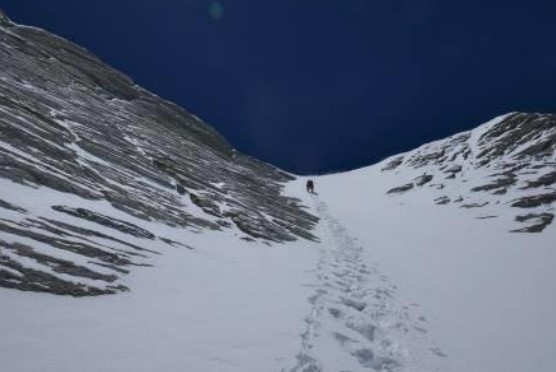 A cimber up a snow couloir leading to a ridge.