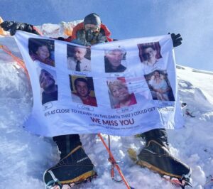 Mitch Hutchcraft holds a banner with photos of relatives and friends perished, on the summit of Everest, in a sunny but windy day.