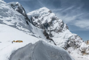 Some tents on a snowy shoulder at the base of Spantik