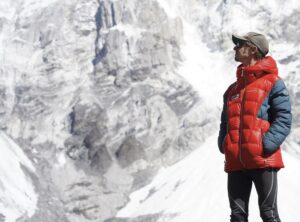 Tyler Andrews in dawn jacket and baseball cap with a rock and ice wall behind.