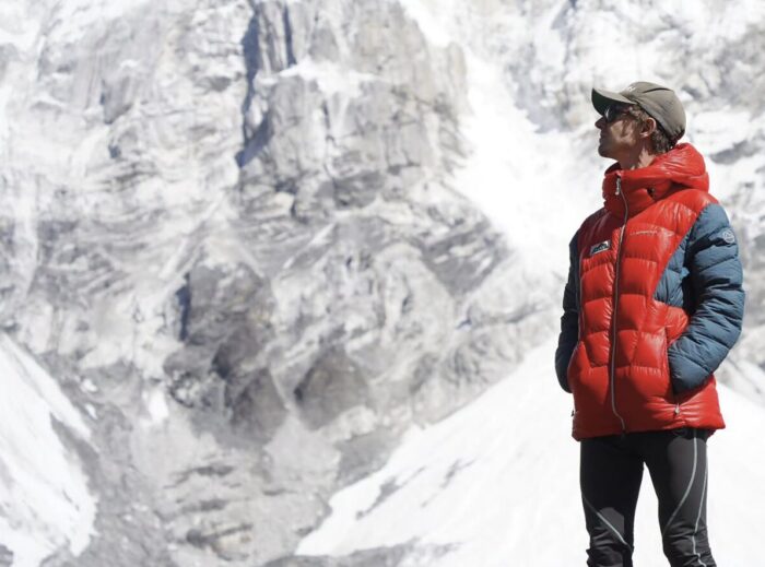 Tyler Andrews in dawn jacket and baseball cap with a rock and ice wall behind.