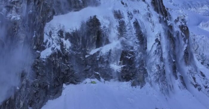 A tent under a rocky face swept by spindrift