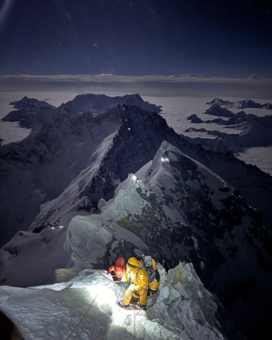 Climbers lit by their headlamps on the final ridge section of Everest, as the sun raise at their back.