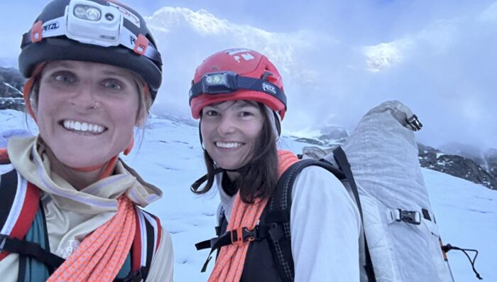 Female climbers Manner and Dvorak smile to the camera with ropes, climbing helmets and head lamps.