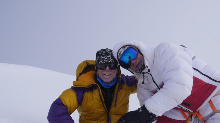Climbers on a snowy summit in thick fog.