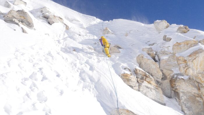 A climber rappells down a snowly steep slope.