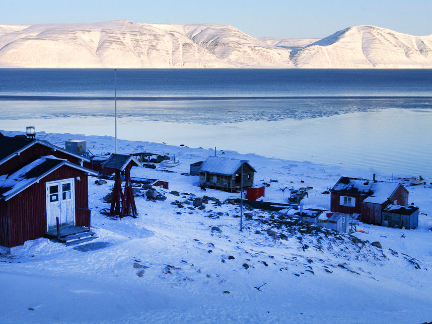 shadowed village hourses with snowy mountains and sea in background.
