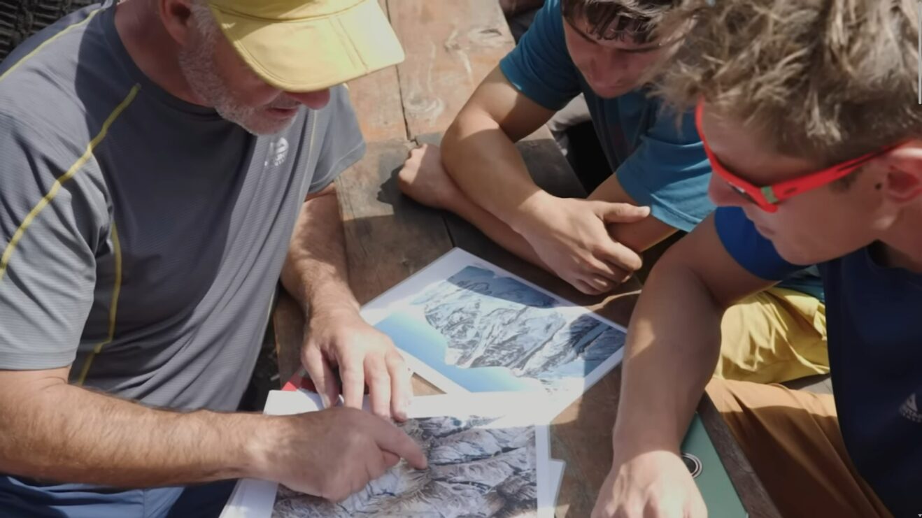 Three men gathered around and gesturing to satellite photo print outs