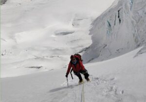 A climber clipped to fixed ropes on a steep snow slope with a serac at his side.
