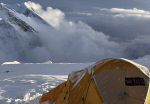 A yellow tent in the snow on Kangchenjunga, clouds wrapping mountains around and below.
