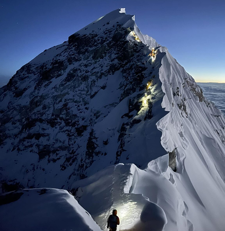 Lights of climbers' headlamps along the summit ridge of Everest, as the sun dawns in the horizon.