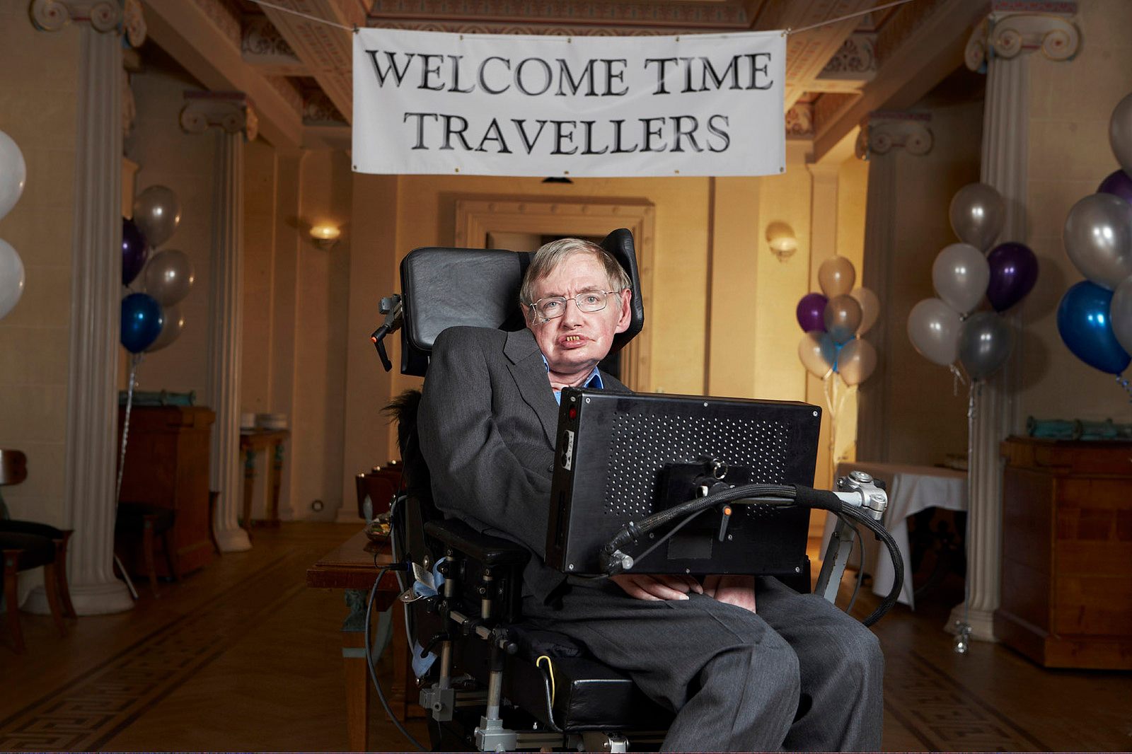 A photo of a man in a wheelchair in front of a balloon-strewn room. A banner reads "Welcome time travellers."