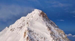A small group of climbers in line, looking tiny on the final ramp leading to the summit of Everest, from Tibet.