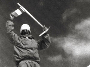 old black and white photo of climber with ice ax over his head