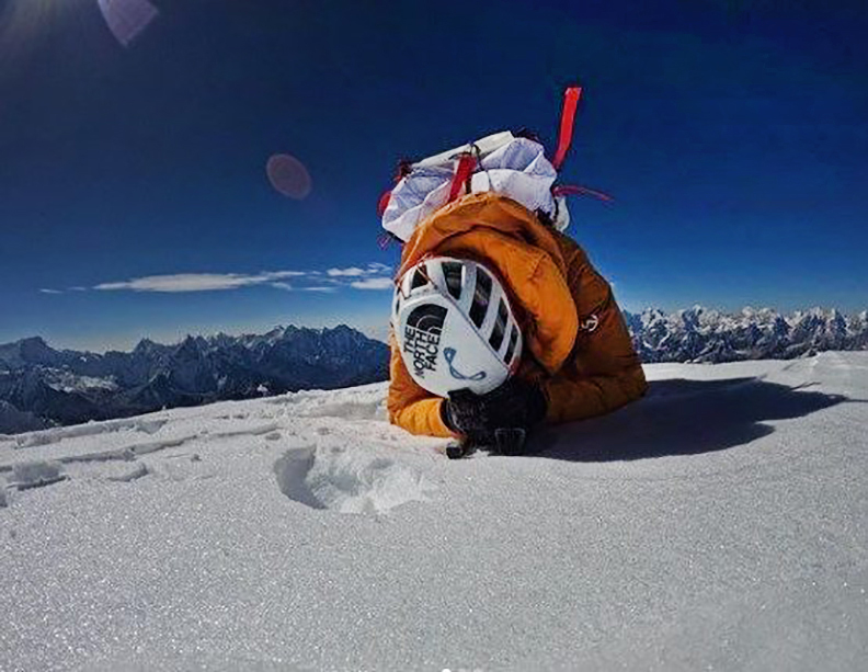 climber kneeling on summit of snowy peak