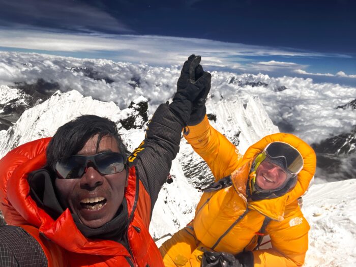Climbers raise their hand in triumph on a summit.