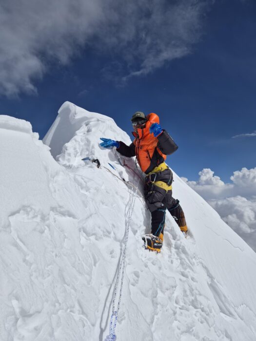 A sherpa guide fixes ropes to the top of a corniced, snowy ridge on Nuptse.