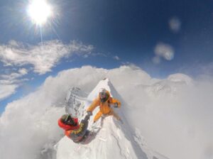 A climber sits on the edge of a sharp summit ridge and shakes hand with sherpa guide.