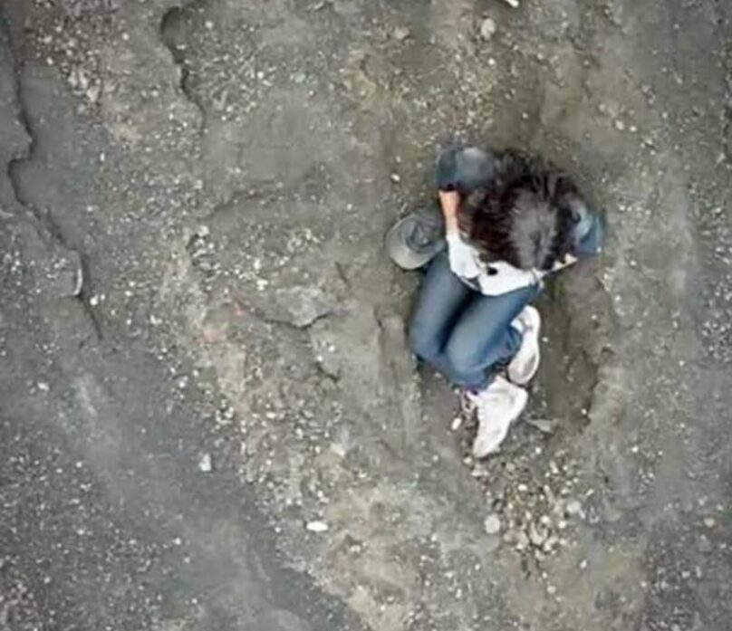 Aerial footage of a woman sitting in ashy dirt