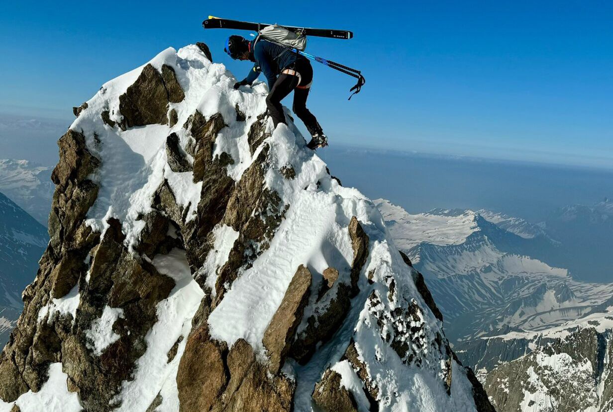 Nicolas Jean climbs to the top of a rocky spire on Mont Blanc, with skis on his back.