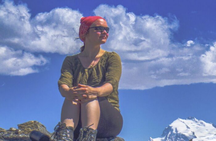 MArie Saame with a blouse and vintage-looking mountain boots, sitting on a rock with a red scarf on her head.