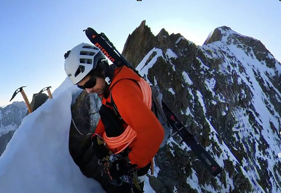 A climber on the sharp summit of Pointe Marguerite, Grandes Jorasses, at dawn, with skis on the back.