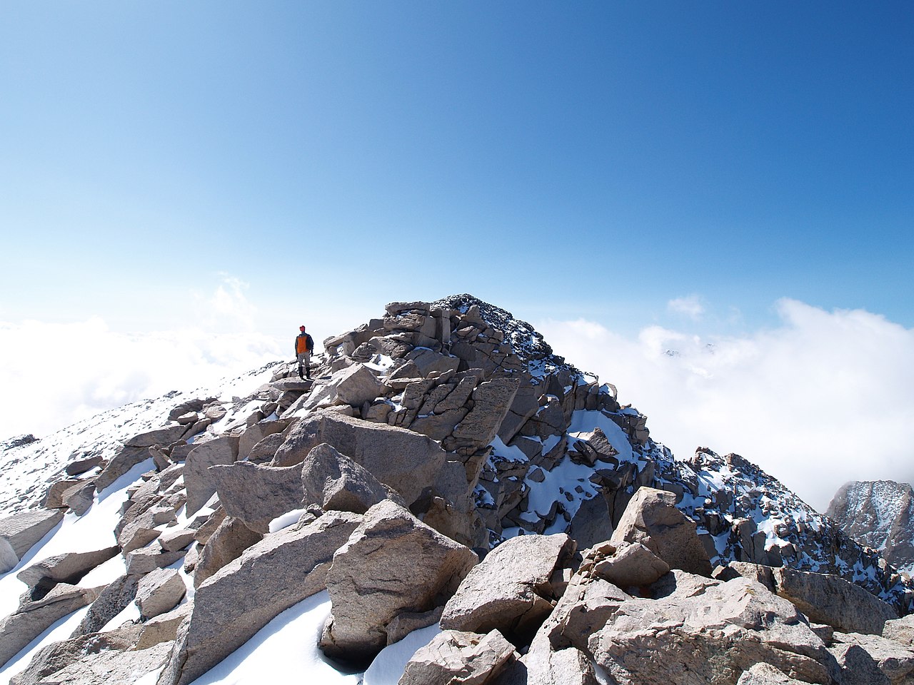 A figure standing on the snow-dusted summit of a rocky peak