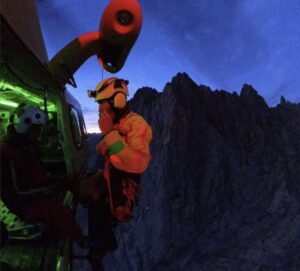 A rescuer hanging from a helicopter flying in a mountain area in the night.