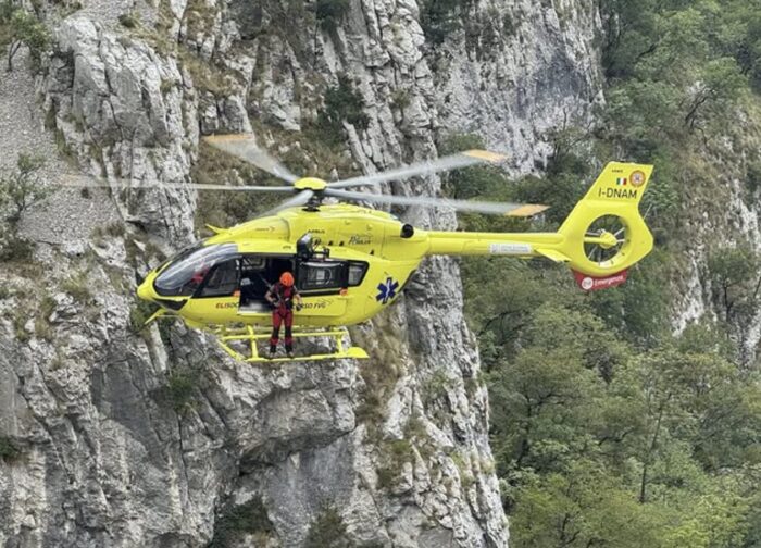 A rescuers stands on the side of a flying helicopter.