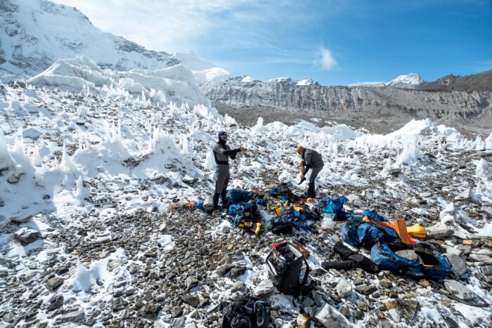 Climbers with all their gear spread on rocky ground, surrounded by penitent ice formations.