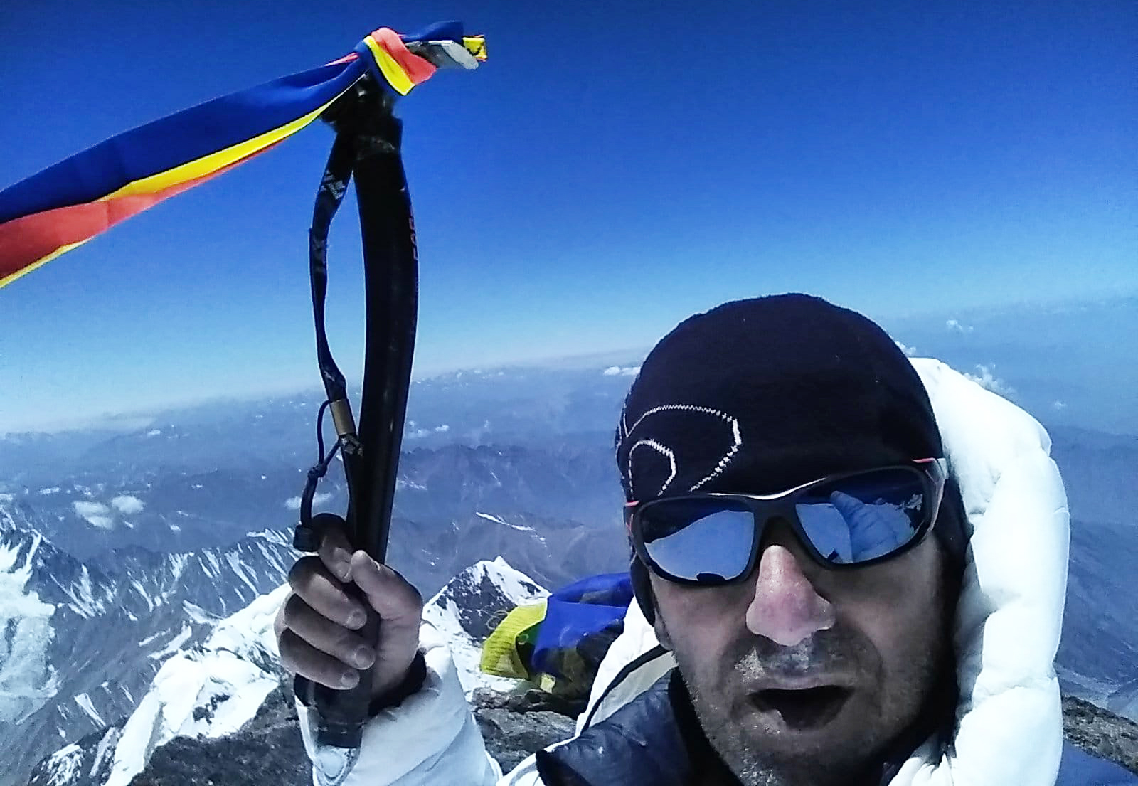 Close shot (selfie) of Horia Colibasanu on the summit, holding an ice-axe with a ribbon colored as the Romanian flag.