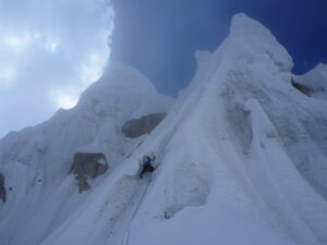 A climber on a vertical section of ice gullies leading to a summit.